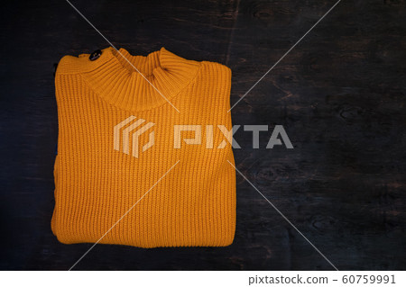 Folded yellow knitted sweater on a dark wooden Folded yellow knitted sweater on a dark wooden 60759991