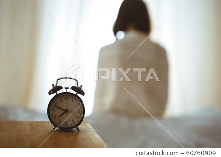 Woman stretching hands in bed after wake up, sun flare . Brunette entering a day happy and relaxed after good night sleep and back view. Concept of a new day and joyful weekend 60760909