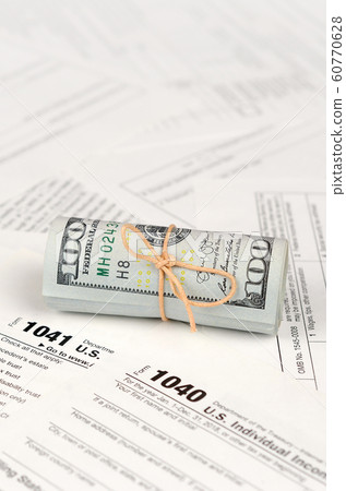 Tax forms lies near roll of hundred dollar bills. Tax forms lies near roll of hundred dollar bills. 60770628