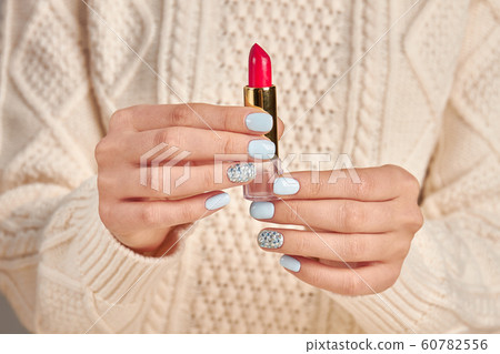 Woman's hand holds a bright red lipstick. 60782556