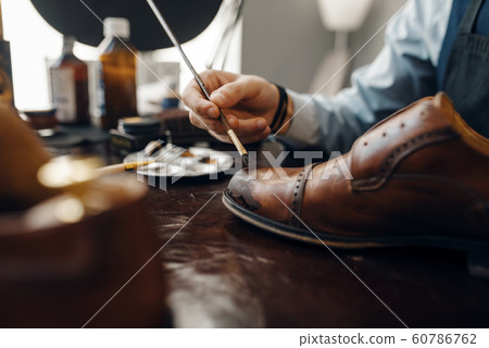 Bootmaker with brush tints shoes, footwear repair 60786762