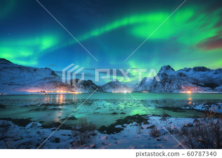 Aurora borealis over the sea coast, snowy mountains and city lights at night. Northern lights 60787340