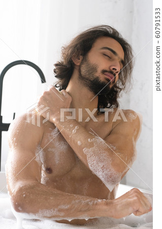 Young muscular man with closed eyes washing his body while having bath 60791533