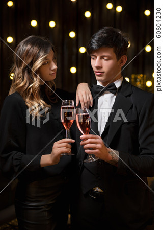 Elegant couple toasting the New Year with champagne and joy as they clink glasses against strings of twinkling party lights Elegant couple toasting the New Year with champagne and joy as they clink glasses against strings of twinkling party lights 60804230