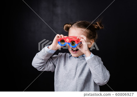 Excited adorable little girl in casualwear holding binoculars by her eyes 60806927