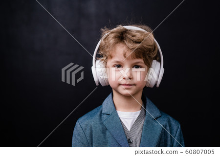 Cute little boy in casualwear listening to music in white headphones 60807005