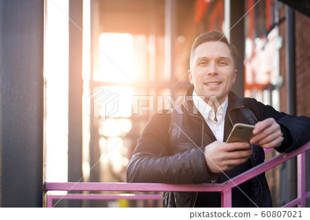 Man looking at camera with phone in hands standing on purple stairs against background of modern building 60807021