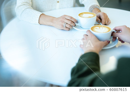 Hands of two young friendly women having cappuccino by table in cafe 60807615