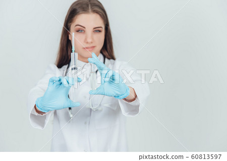 Smilng young female doctor showing to the camera two syringes, narroving her eyes. 60813597