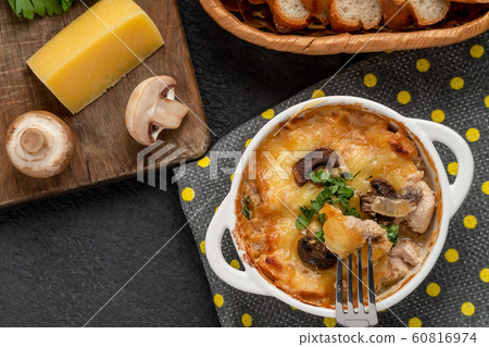 Casserole with chicken, mushrooms and cheese, known in Russia as julienne in white bowl with herbs on a kitchen towel, top view, flat lay Casserole with chicken, mushrooms and cheese, known in Russia as julienne in white bowl with herbs on a kitchen towel, top view, flat lay 60816974