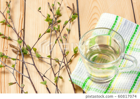 Birch juice on kitchen towel on a wooden table in a glass mug, next to a branch of birch with young leaves Birch juice on kitchen towel on a wooden table in a glass mug, next to a branch of birch with young leaves 60817074
