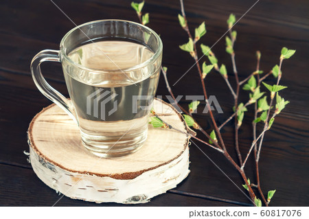 Birch juice on a dark table in a glass mug, next to a branch of birch with young leaves Birch juice on a dark table in a glass mug, next to a branch of birch with young leaves 60817076