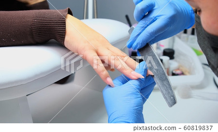 Manicurist files a nail with a nail file to a client. Manicure process, nail extension. close-up 60819837