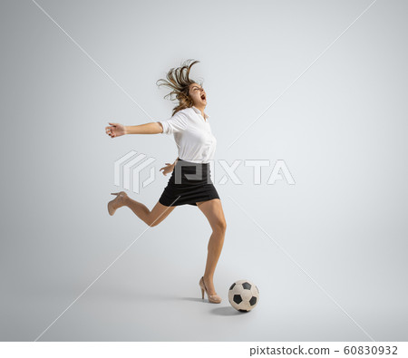Caucasian woman in office clothes kicking ball isolated on grey studio background Caucasian woman in office clothes kicking ball isolated on grey studio background 60830932