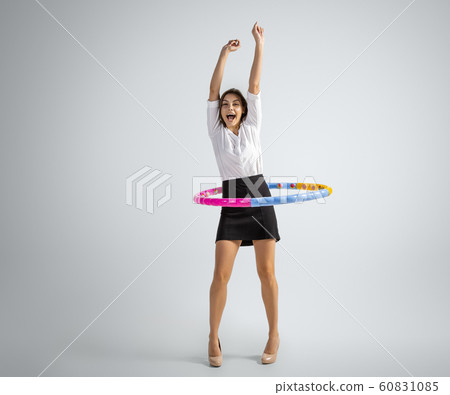 Caucasian woman in office clothes training with hoop isolated on grey studio background Caucasian woman in office clothes training with hoop isolated on grey studio background 60831085