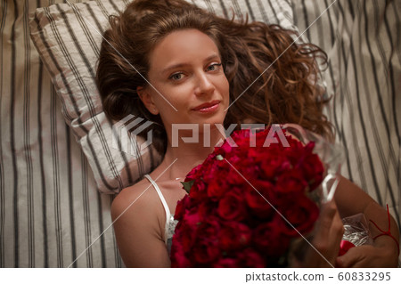 Good morning Attractive young woman in bed is holding bouquet of hundred red roses. Good morning Attractive young woman in bed is holding bouquet of hundred red roses. 60833295