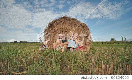 Happy large family sits near a sheaf of straw in the field. 60834003