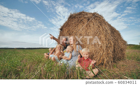 Happy large family sits near a sheaf of straw in the field. Happy large family sits near a sheaf of straw in the field. 60834011