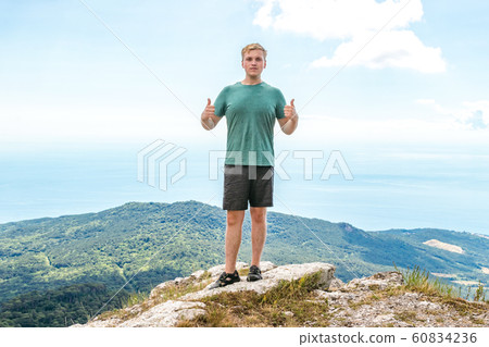 Young man standing on top of cliff in mountains 60834236