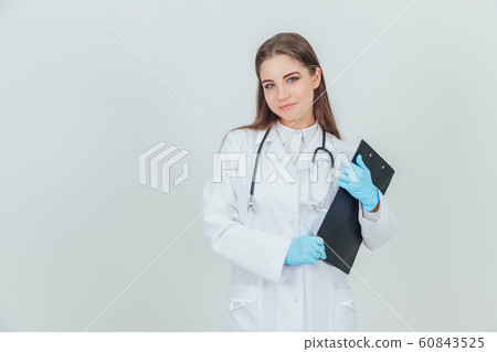 Happy young female intern standing in medical uniform, holding clipboard, smiling lovely. 60843525