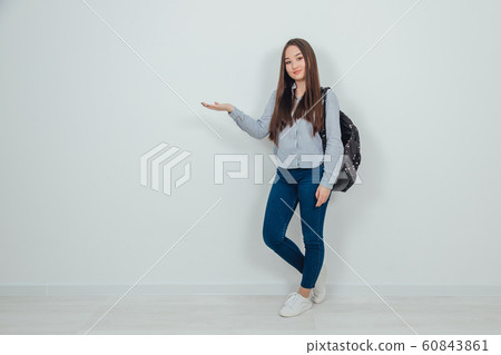 Inspired young asain girl standing with backpack slung over her shoulder, raising opened palm with copyspace for text or product. 60843861