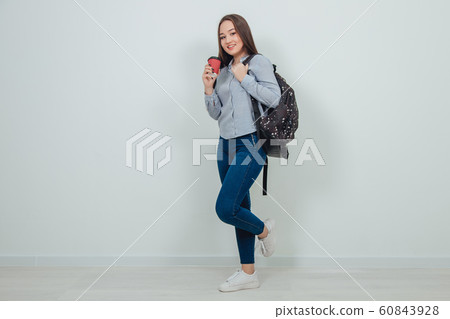 Young beautiful asian student girl standing with a backpack holding a cup of coffee. 60843928