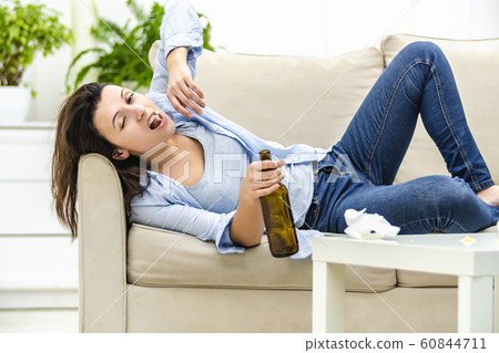 Drunk woman is laying on the sofa, holding an empty bottle. Woman is making faces. Close up. Drunk woman is laying on the sofa, holding an empty bottle. Woman is making faces. Close up. 60844711