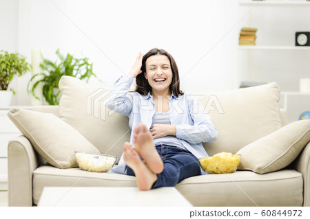 Beautiful smiling woman is watching TV at home with popcorn and potato chips snacks. Beautiful smiling woman is watching TV at home with popcorn and potato chips snacks. 60844972