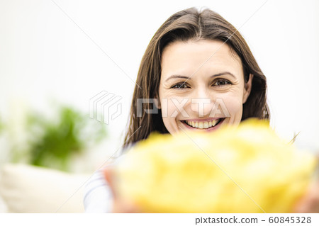 Happy adorable brunette women offers a large deep plate with potato chips snack. Blurred forefront. 60845328