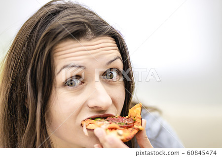 Attractive brunette woman wants to eat pizza slice, looking at it, on light background. Close up. Copy space. 60845474