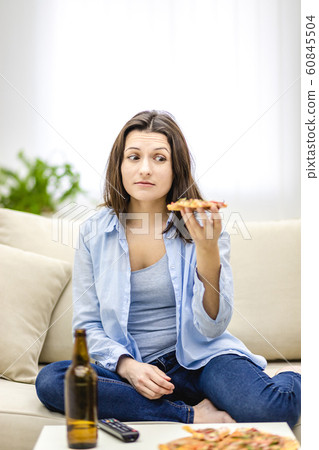 Brunette woman looks at a slice of pizza with disgust. Hard choice. Brunette woman looks at a slice of pizza with disgust. Hard choice. 60845504