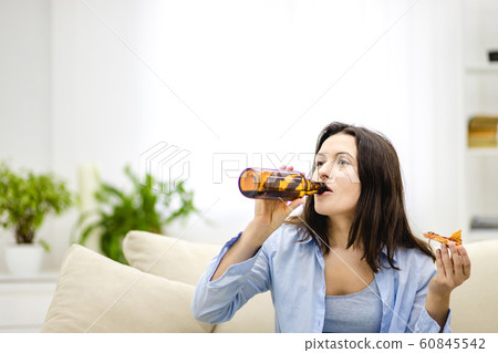 Pleased, attractive woman drinks beer and holds a slice of pizza in the other hand. Isolated woman on blurred light background. Copy space. Close up. 60845542