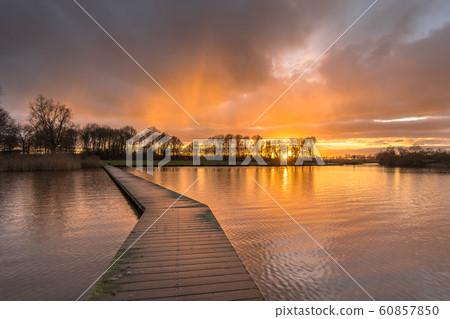 Wooden walkway in lake under orange sunset 60857850