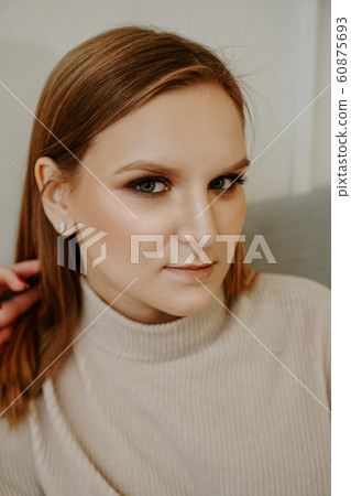 Portrait of Woman dressed in beige sweater sitting on bed Portrait of Woman dressed in beige sweater sitting on bed 60875693
