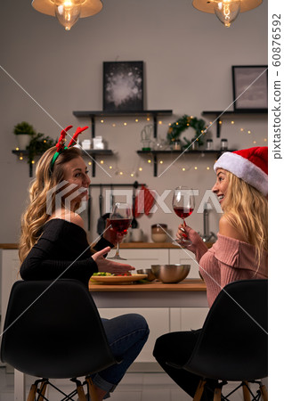 Curly girls sitting at festive table with wine glasses in kitchen at Christmas. 60876592