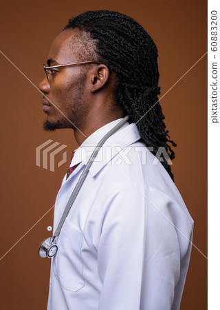 Young handsome African man doctor against brown background Young handsome African man doctor against brown background 60883200