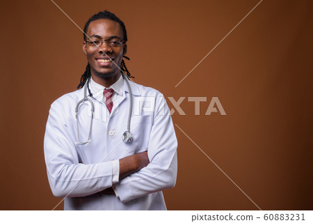 Young handsome African man doctor against brown background Young handsome African man doctor against brown background 60883231