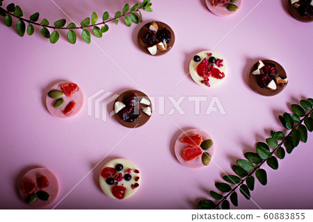Small brown and pink round chocolates and branches lie on a pink background. 60883855