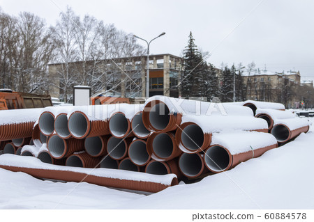 Sewer pipes lie on a construction site, covered with snow 60884578