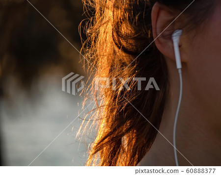 A girl with with beautiful sunlight in hairs is listening music with earphones. No face. 60888377