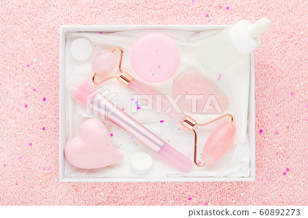 beauty box with rose quartz jade roller and stone, face serum and brush on pastel pink background 60892273