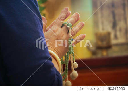 Woman press the hands together at the chest in sign of respect and hold prayer beads on hands for praying with shrine on background Woman press the hands together at the chest in sign of respect and hold prayer beads on hands for praying with shrine on background 60899060