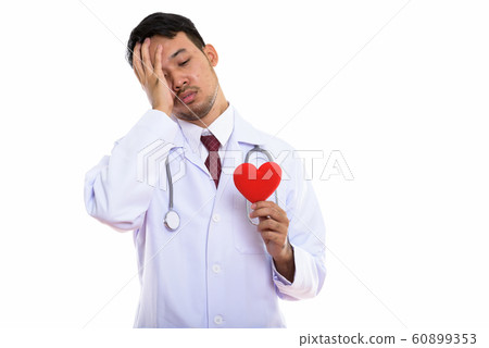 Studio shot of young Asian man doctor holding red heart while lo Studio shot of young Asian man doctor holding red heart while lo 60899353