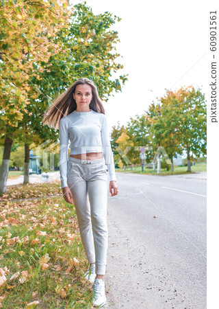 Beautiful girl in autumn in park, walks by road. Resting weekend in park. Emotions of comfort are pleasure and enjoyment. Walk on autumn day, warm casual clothes, background trees leaves. Beautiful girl in autumn in park, walks by road. Resting weekend in park. Emotions of comfort are pleasure and enjoyment. Walk on autumn day, warm casual clothes, background trees leaves. 60901561