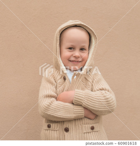 Little boy 3-5 years old, in a beige sweater with a hood, happy smiling, cheerful and joyful. Background wall, autumn on the street. Emotions of pleasure and fun. Little boy 3-5 years old, in a beige sweater with a hood, happy smiling, cheerful and joyful. Background wall, autumn on the street. Emotions of pleasure and fun. 60901618