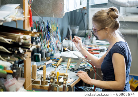Woman artist making glass jewelry in her workshop Woman artist making glass jewelry in her workshop 60905674