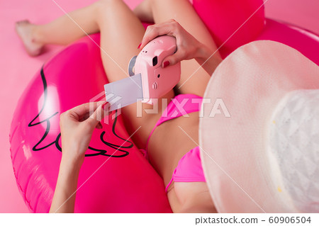 The girl in a swimsuit lies on an inflatable flamingo looking at the photo 60906504