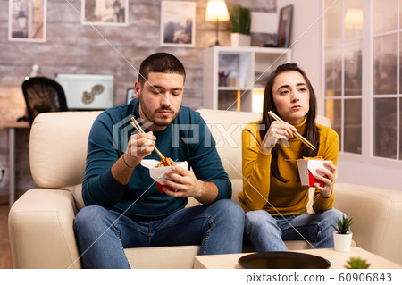 In modern cozy living room couple is enjoying takeaway noodles while watching TV 60906843