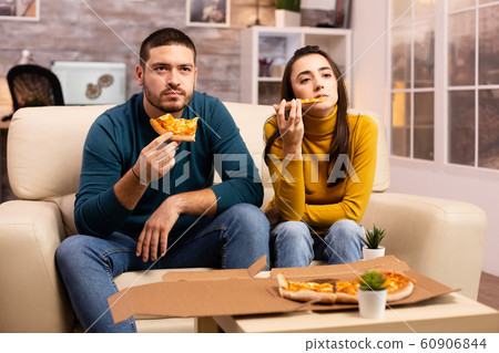 Gorgeous young couple eating pizza while watching TV Gorgeous young couple eating pizza while watching TV 60906844
