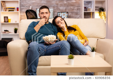 Handsome couple at home eating pop corn and watching TV 60906856